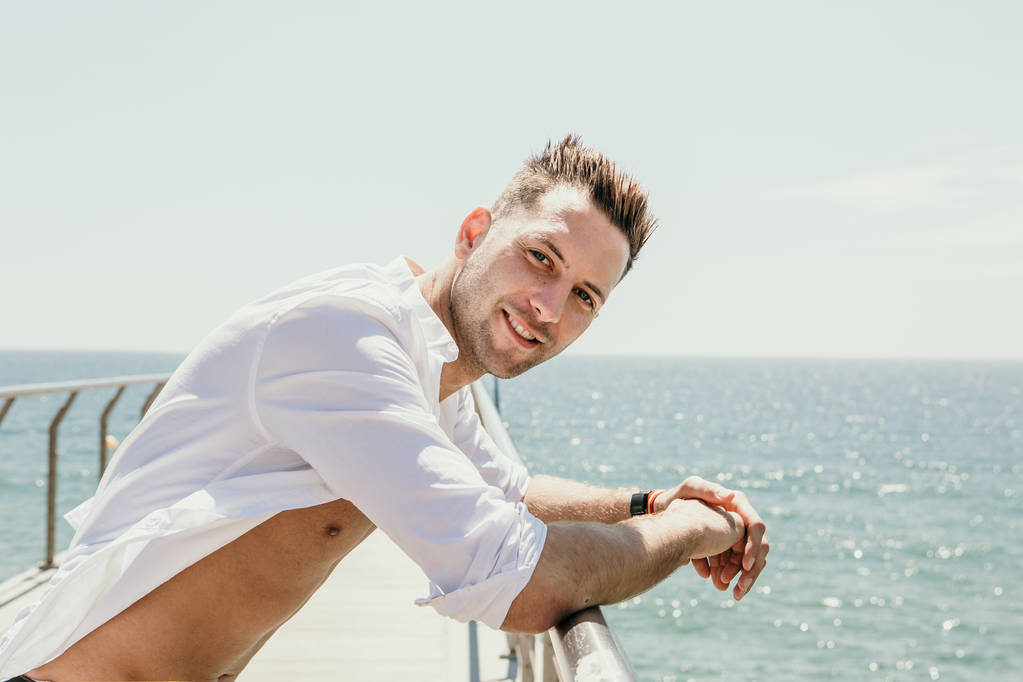 Beau jeune homme souriant heureux portant une chemise blanche à la mer ou sur le fond océanique.
. - Photo, image
