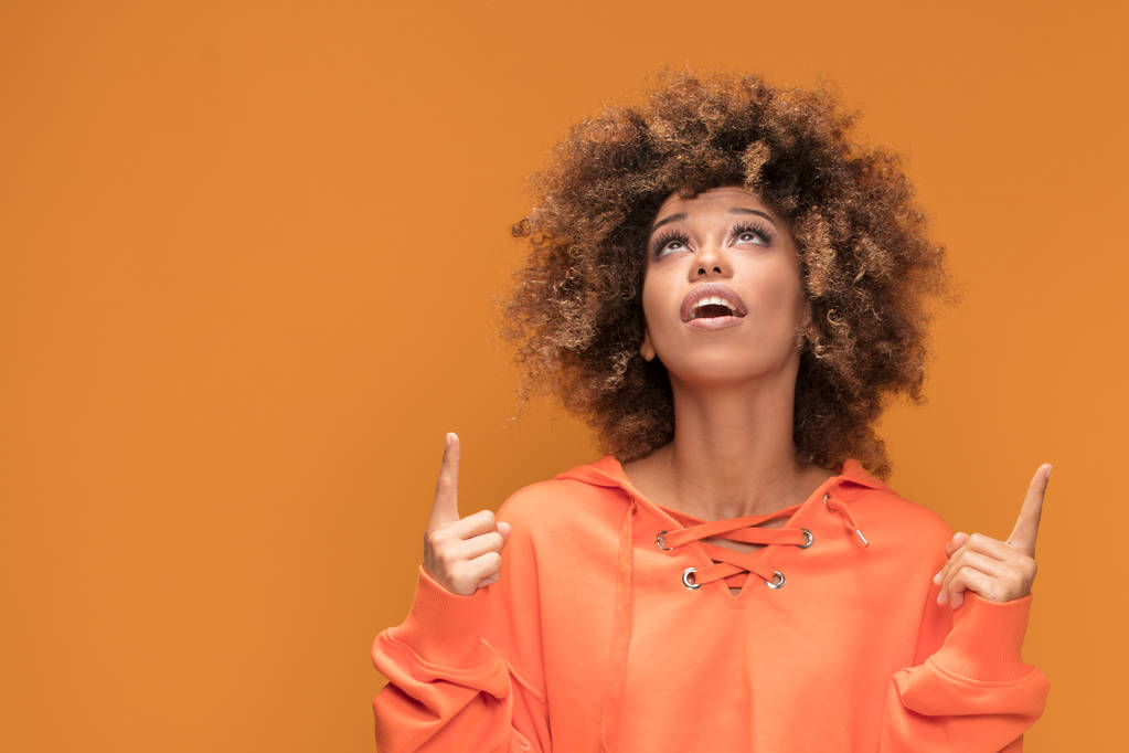 Foto van een Afrikaanse Amerikaanse vrouw met glamour make-up en afro kapsel gekleed in modieuze korte oranje blouse. Meisje opzoeken . - Foto, afbeelding