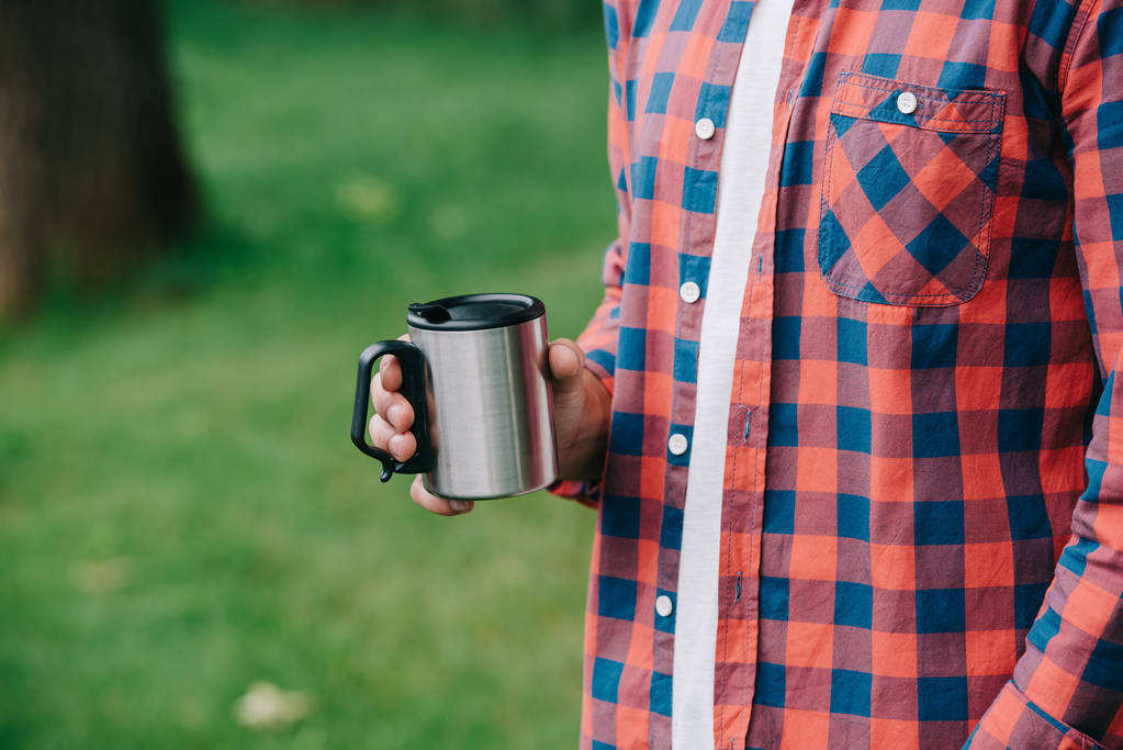屋外のマグカップを保持している格子縞のシャツの若い男のクロップ撮影  - 写真・画像