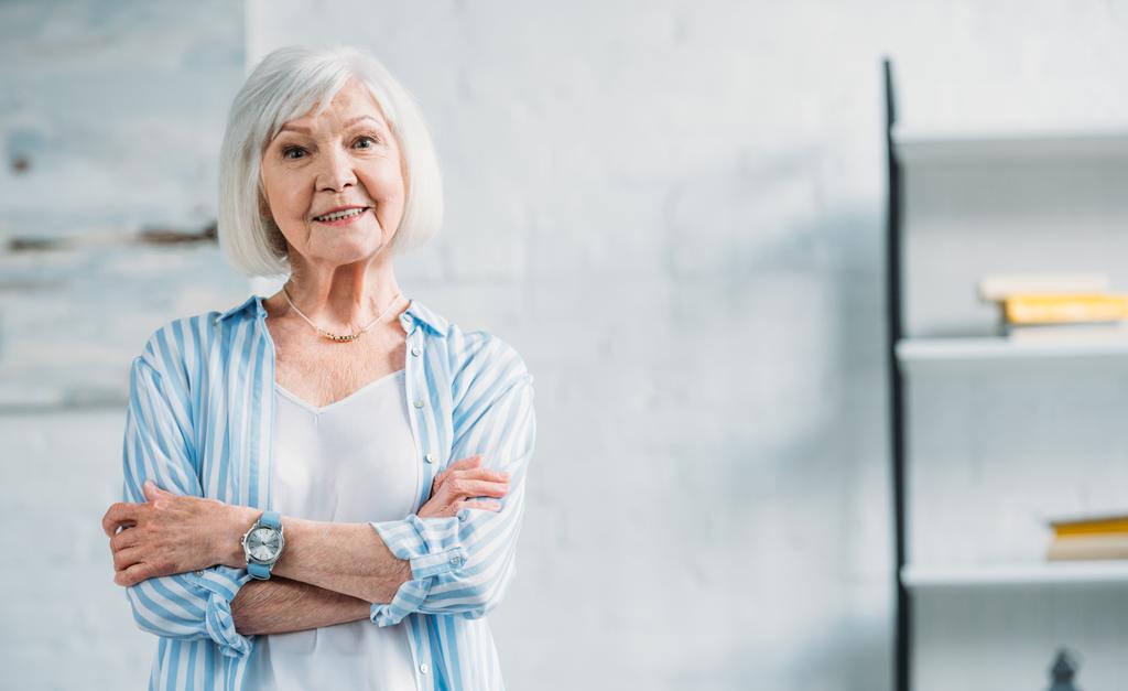 portrét krásné usměvavé starší dáma ve stylovém oblečení s rukama zkříženýma na kameru doma - Fotografie, Obrázek
