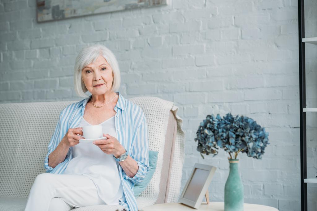 пожилая женщина с чашкой ароматного кофе отдыхает на диване дома
 - Фото, изображение