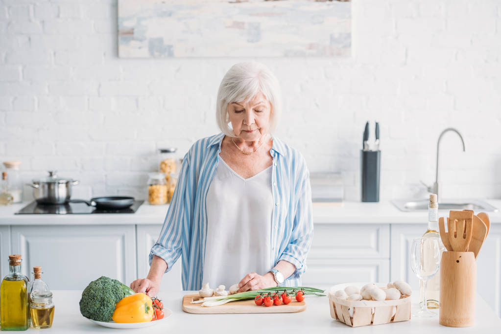 портрет старшої леді, що ріже овочі під час приготування вечері за лічильником на кухні
 - Фото, зображення
