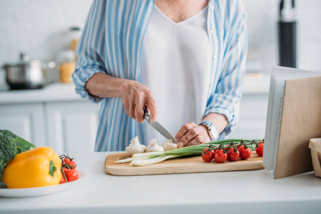 Teilansicht einer Seniorin beim Pilzschneiden beim Kochen am Tresen in der Küche - Foto, Bild
