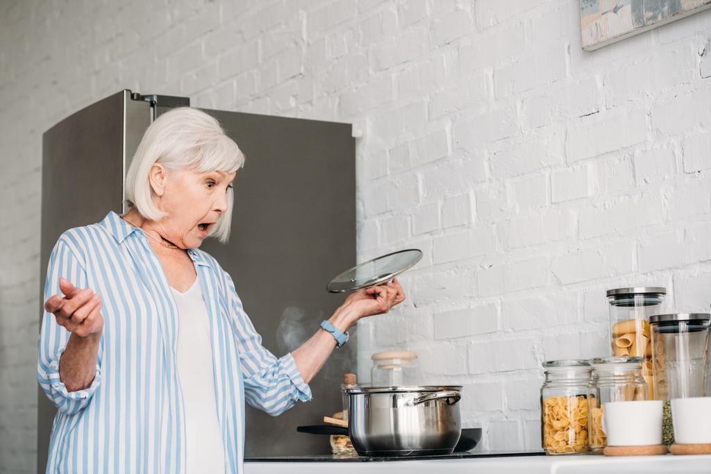 vista laterale di scioccato signora anziana controllo casseruola sul fornello in cucina
 - Foto, immagini