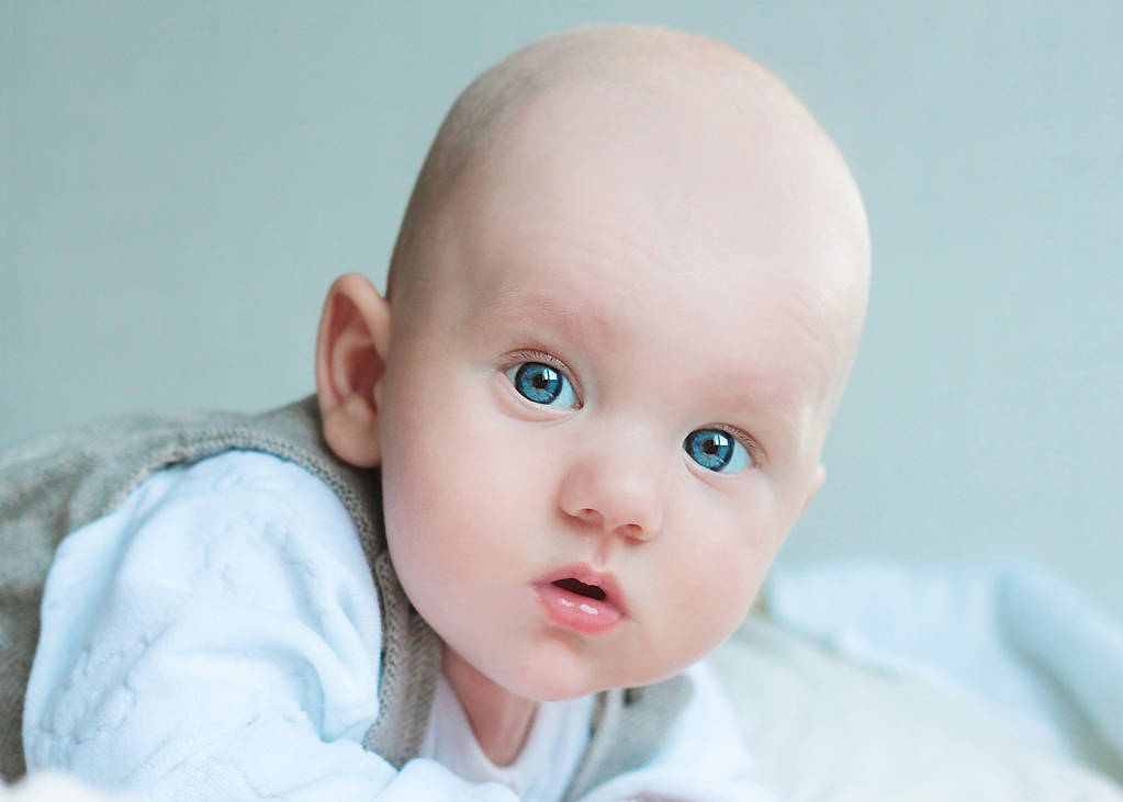bebé con grandes ojos azules se viste con un chaleco descansa sobre su estómago
 - Foto, Imagen
