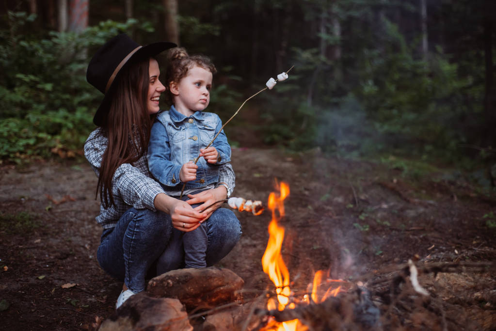 mother and daughter roast marshmallow candies on the campfire in forest. Spring or autumn camping - Photo, Image
