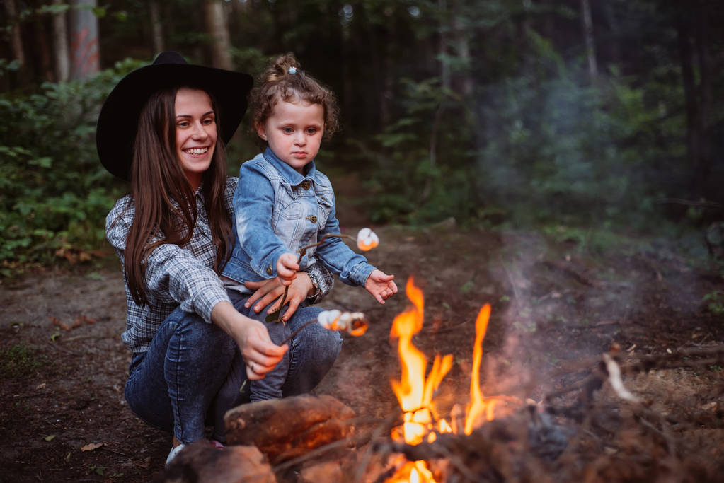 madre e figlia arrostiscono caramelle marshmallow sul falò nella foresta. Primavera o autunno campeggio
 - Foto, immagini