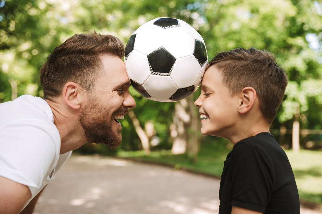 幸せな若い父の絵は、サッカー ボールと公園の自然の中屋外彼の幼い息子と楽しい時を過す. - 写真・画像