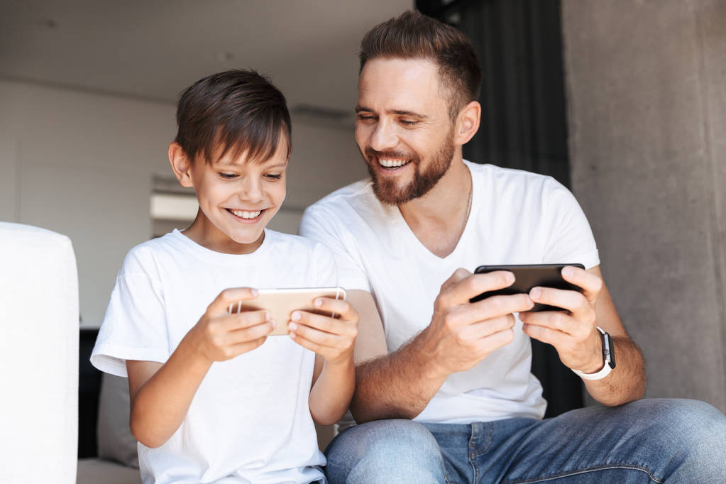Image de bel homme barbu à l'intérieur à la maison avec son fils enfant jouer à des jeux par téléphones mobiles
. - Photo, image