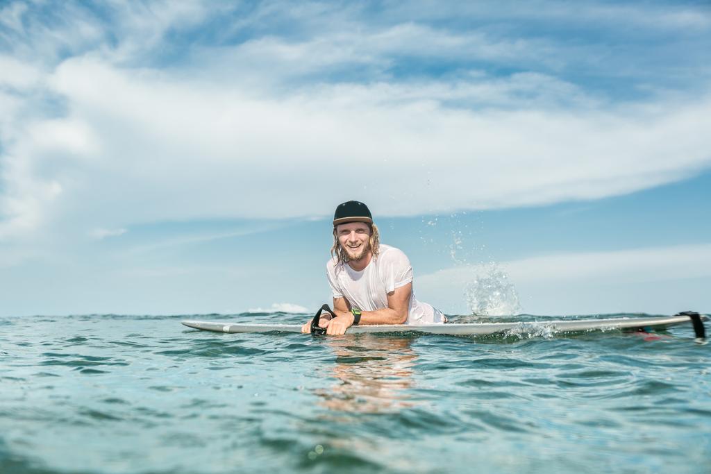 smiling male surfer resting in ocean with surfing board at Nusa Dua Beach, Bali, Indonesia - Photo, Image