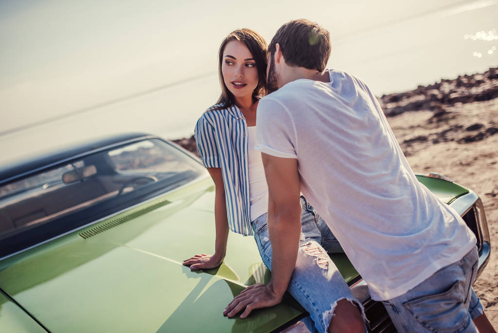 ロマンチックなカップルはビーチでグリーンのレトロな車に近い立っています。ハンサムなひげを生やした男とビンテージ クラシックカーと魅力的な若い女性。愛の物語. - 写真・画像
