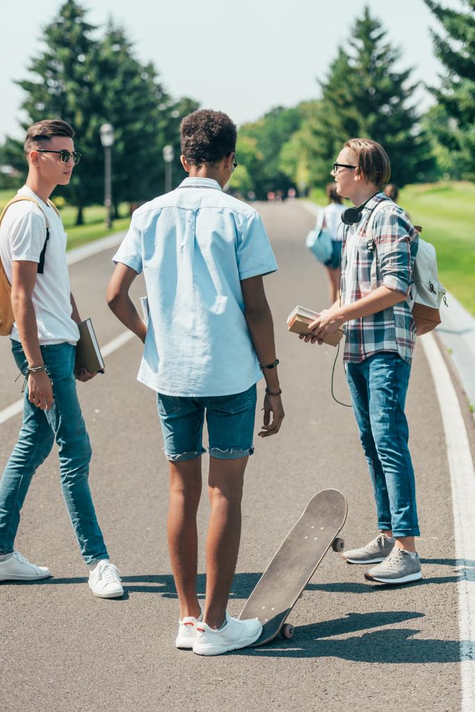 ragazzi adolescenti multietnici con libri e skateboard in piedi e parlando nel parco
 - Foto, immagini