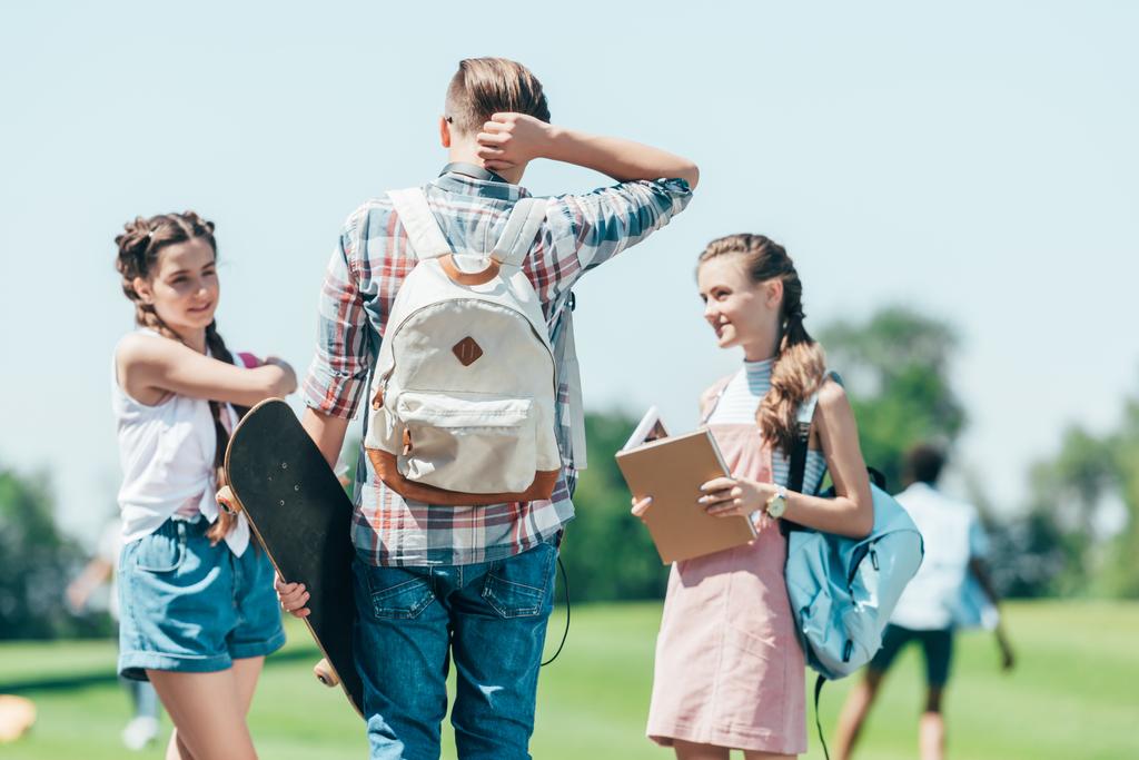 підлітки з книгами і скейтбордом стоять і розмовляють в парку
 - Фото, зображення