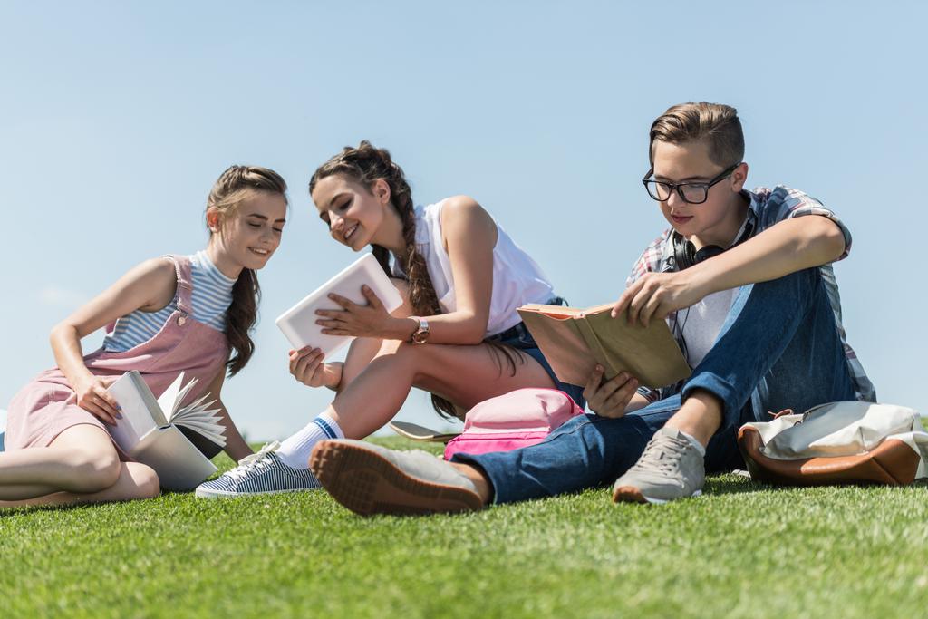 χαμηλή γωνία προβολής της χαμογελούν οι έφηβοι που μελετούν με βιβλία και ψηφιακό tablet στο πάρκο - Φωτογραφία, εικόνα
