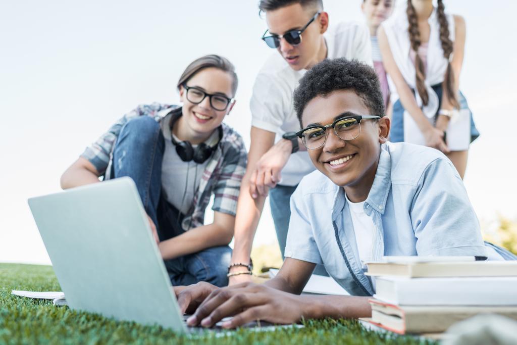 glückliche multiethnische Teenager, die Laptop benutzen und im Park lernen  - Foto, Bild