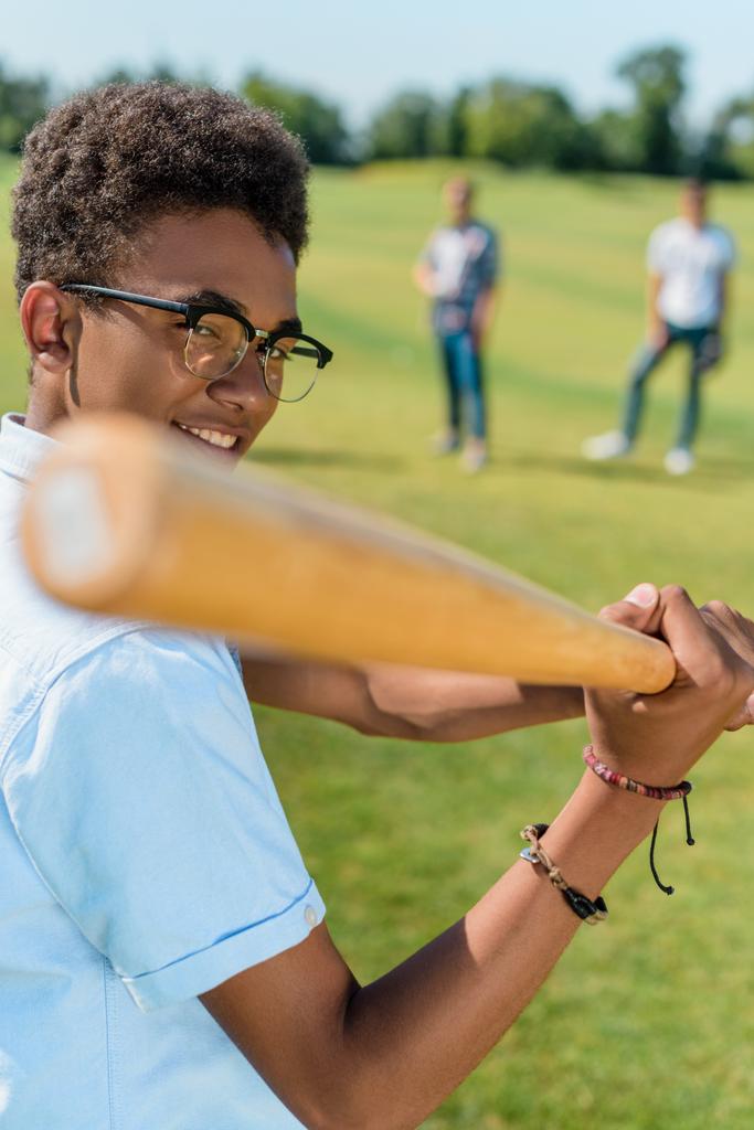 Selektivní fokus usmívající se afrických amerických teenagerů hrát baseball s přáteli v parku - Fotografie, Obrázek