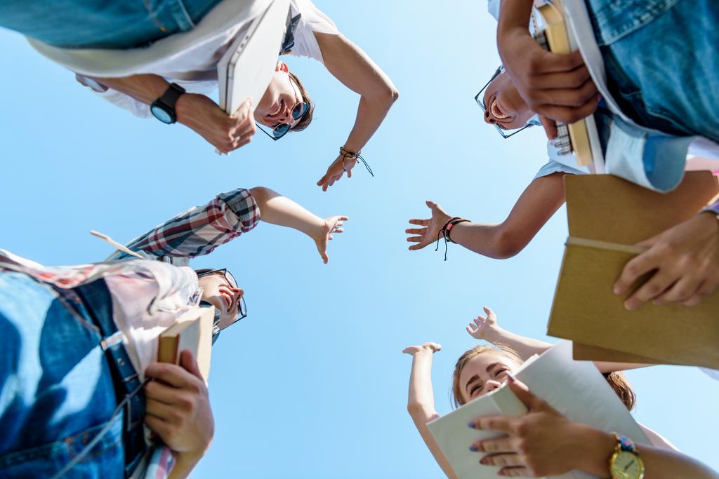 Blick von unten auf glückliche multiethnische Teenager, die High Five im Park geben  - Foto, Bild