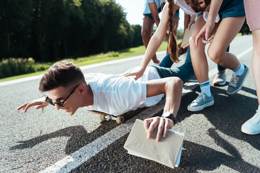 Schnappschuss von Teenagern, die Spaß haben, während Freund auf Skateboard liegt - Foto, Bild