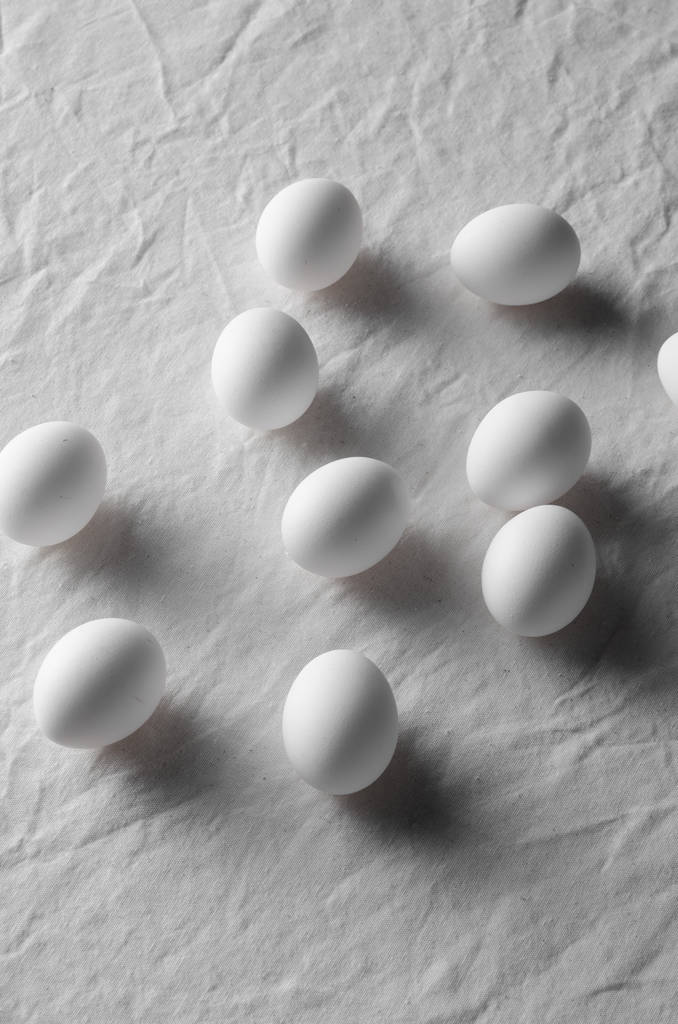 weiße Eier auf einem weißen Leinentischtuch Hintergrund. - Foto, Bild