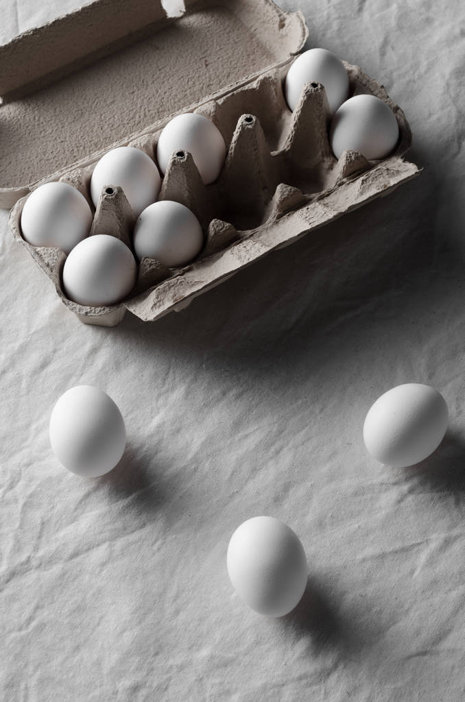 Bir yumurta kartonu beyaz yumurtalar. Beyaz keten masa örtüsü arka plan. - Fotoğraf, Görsel