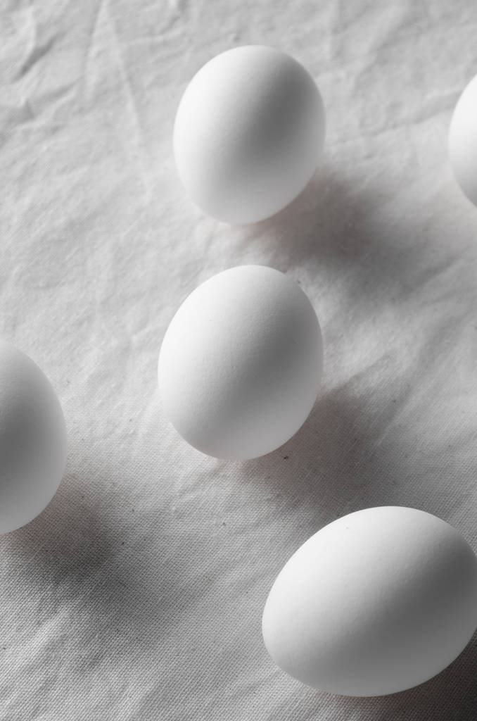 Nahaufnahme von weißen Eiern auf einem weißen Leinentischtuch Hintergrund. - Foto, Bild