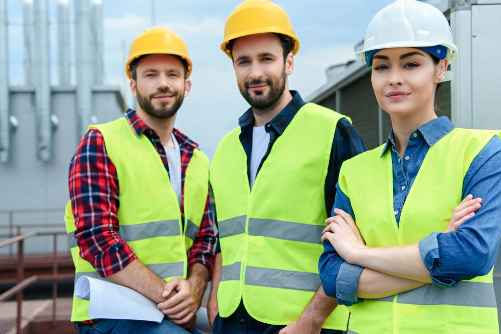 professional engineers in safety vests and hardhats posing with crossed arms - Photo, Image
