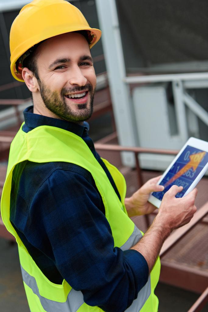smiling architect in safety vest using digital tablet with arrow - Photo, Image