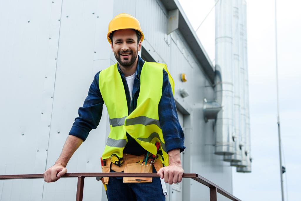 чоловічий усміхнений інженер у жилеті та шоломі з поясом інструментів на будівництві
 - Фото, зображення