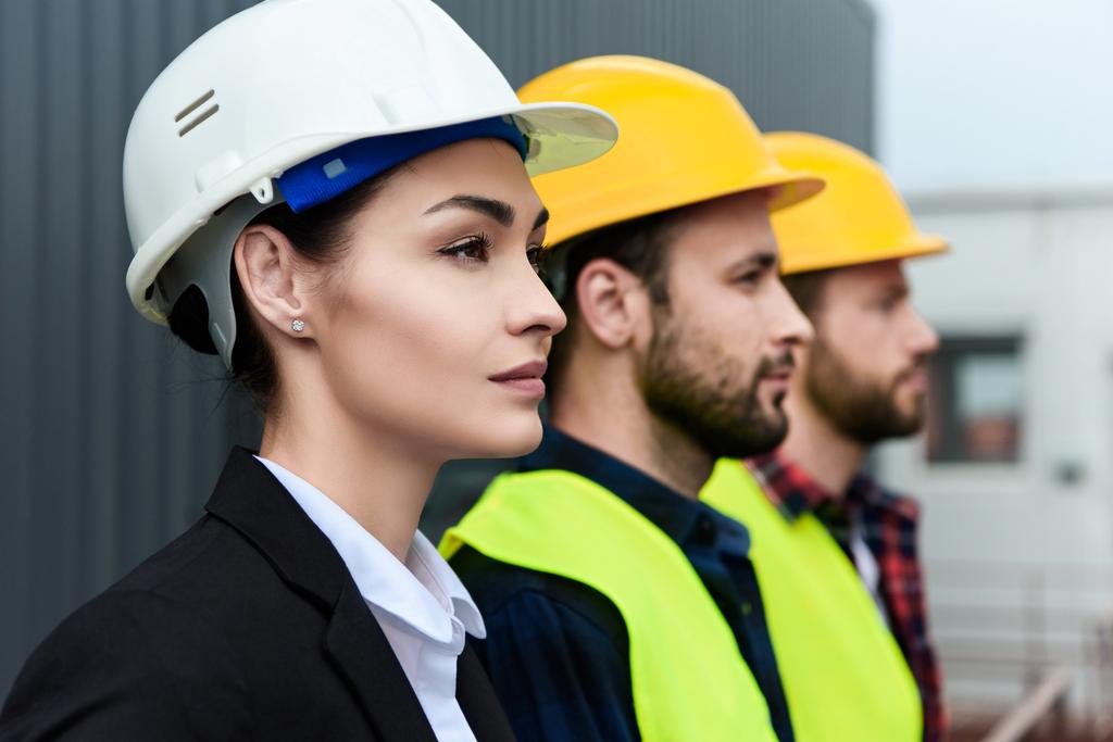 naisinsinööri ja miespuoliset työntekijät kypärissä rakenteilla
 - Valokuva, kuva