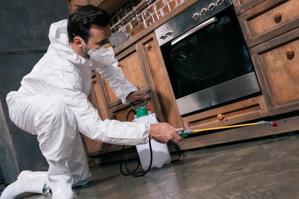 працівник боротьби з шкідниками розпилює пестициди під шафою на кухні
  - Фото, зображення