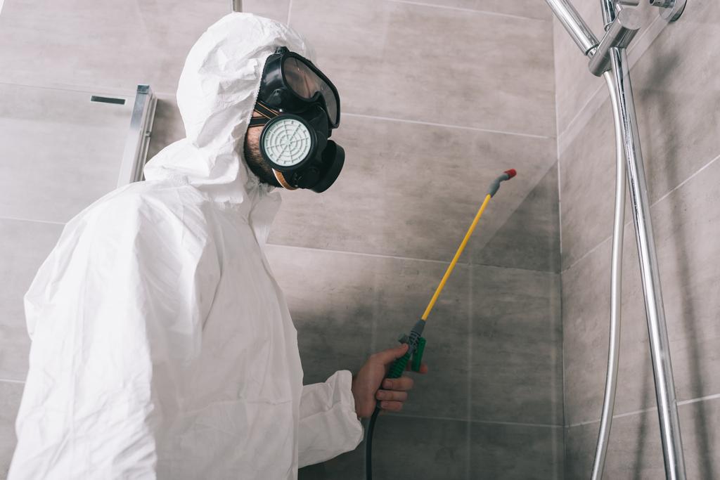 працівник управління шкідниками в респіраторі розпилює пестициди з розпилювачем у ванній кімнаті
 - Фото, зображення
