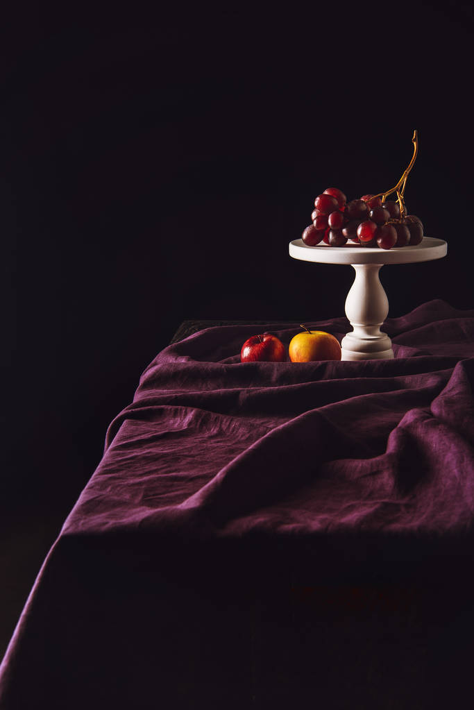 suporte com uvas e maçãs na mesa com cortinas em preto
 - Foto, Imagem