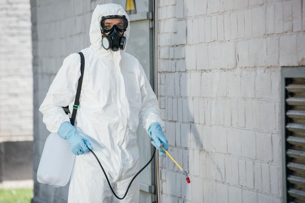 travailleur de la lutte antiparasitaire dans le respirateur pulvérisation de pesticides avec pulvérisateur sur le mur de construction
 - Photo, image