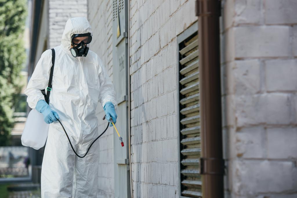 tuholaistorjunta työntekijä ruiskuttamalla torjunta-aineita sumutin rakennuksen seinään kadulla
 - Valokuva, kuva