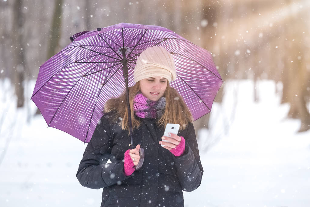 Frau mit Regenschirm nutzt Smartphone und genießt Wintersaison im Park. - Foto, Bild