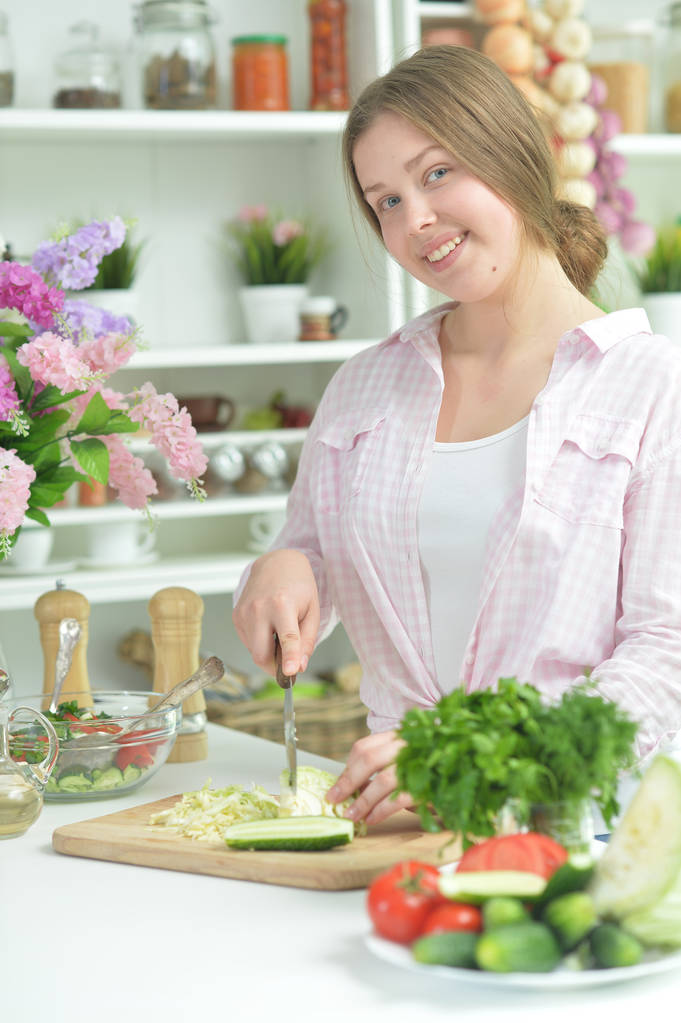 Милая девочка-подросток готовит свежий салат на кухонном столе
   - Фото, изображение