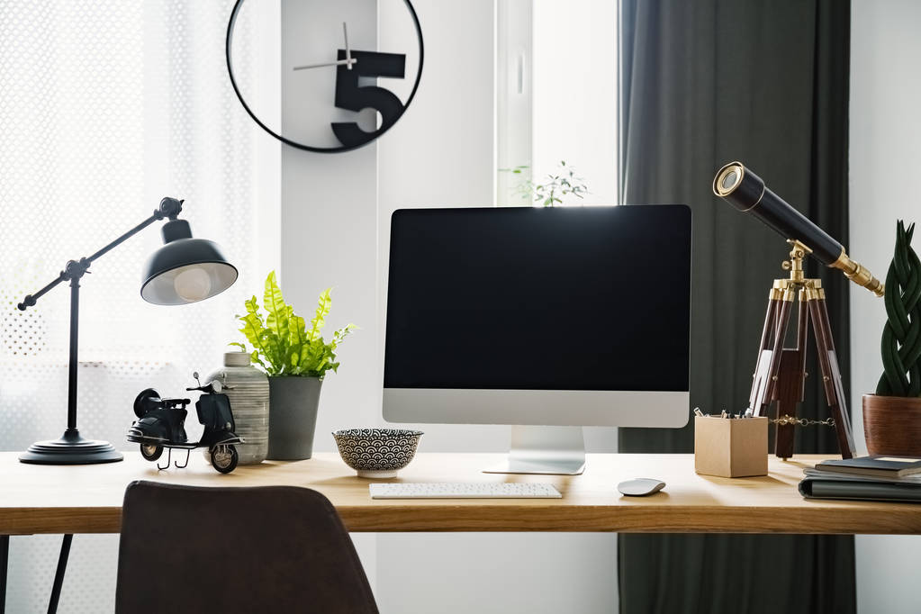 Close-up photo of computer with mockup standing on a wooden desk with vintage telescope, fresh green plants and metal lamp - Photo, Image