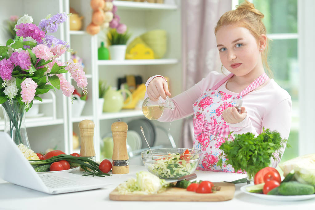 Schattige tiener meisje voorbereiding van frisse salade op keukentafel   - Foto, afbeelding