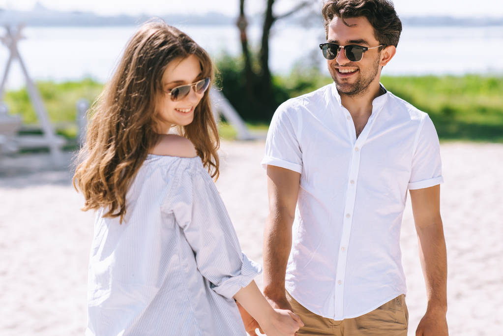 uśmiechający się para w okulary, trzymając się za ręce na głównej plaży miejskiej - Zdjęcie, obraz