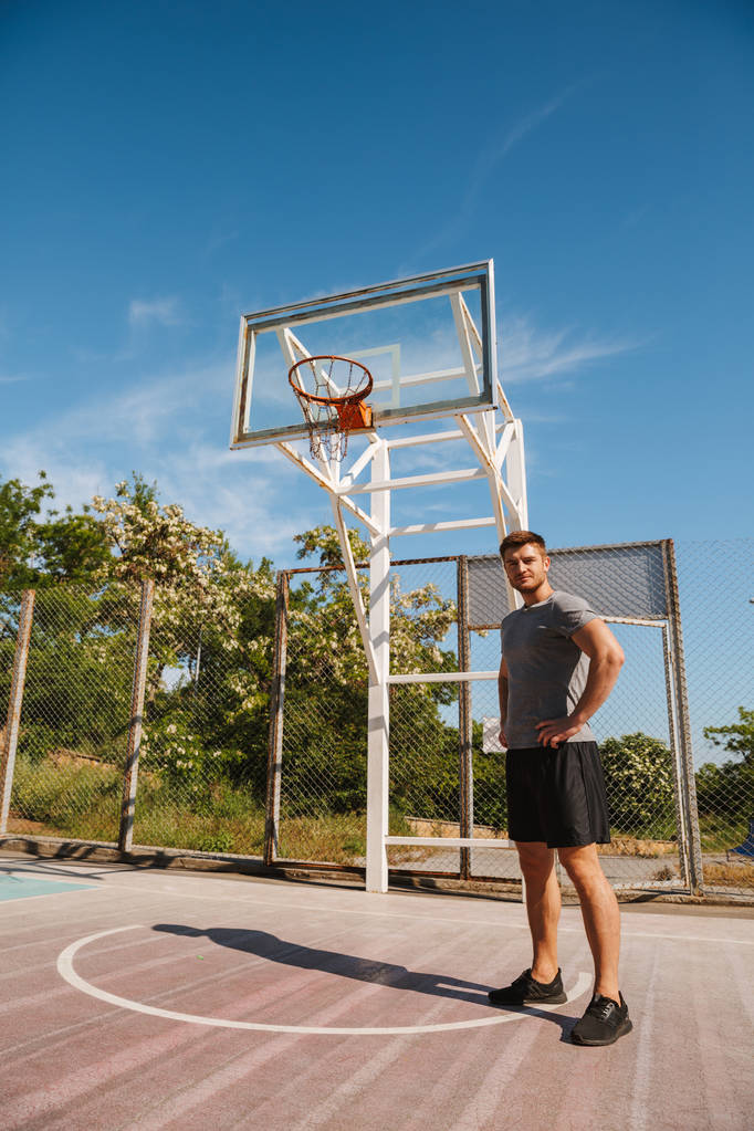 Молодой спортсмен в шортах стоит на улице на баскетбольной площадке
 - Фото, изображение