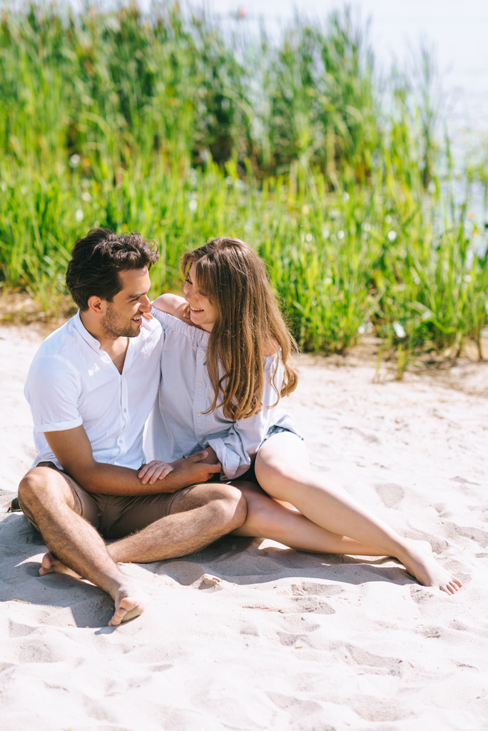 onnellinen pari istuu hiekkarannalla ja katselee toisiaan
 - Valokuva, kuva