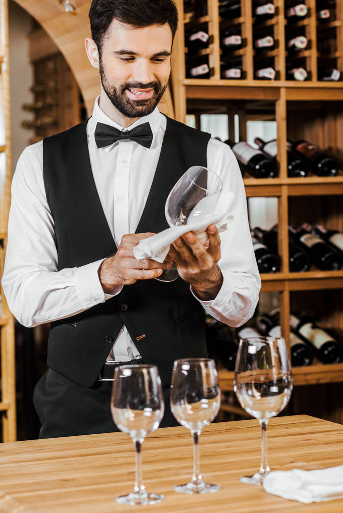 sonriente joven administrador de vino comprobar vidrio limpio en la tienda de vinos
 - Foto, imagen