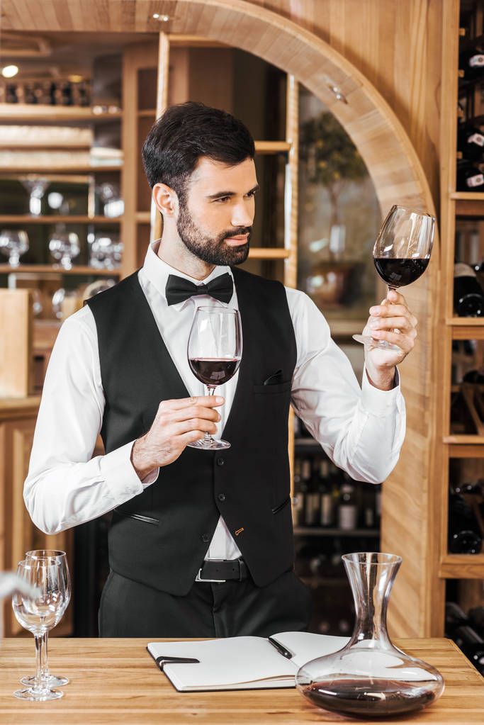 confident young sommelier examining color of wine at wine store - Photo, Image