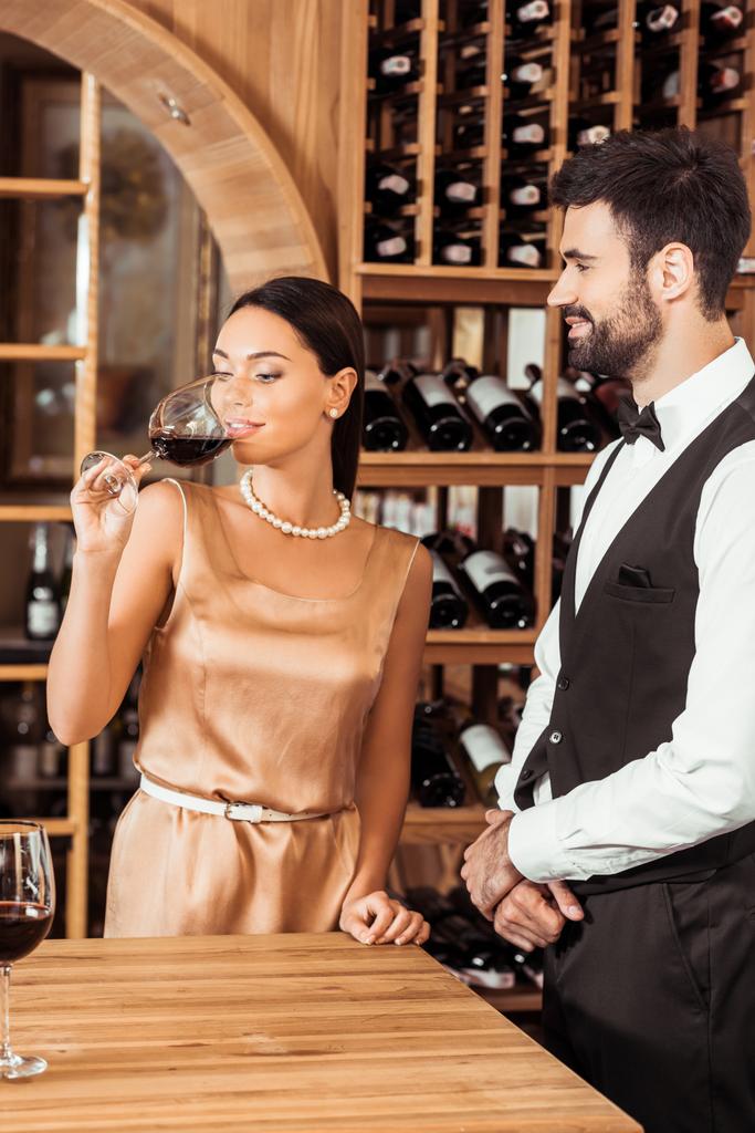 Weinbegleiterin steht neben Frau, während sie Wein im Weinladen probiert - Foto, Bild