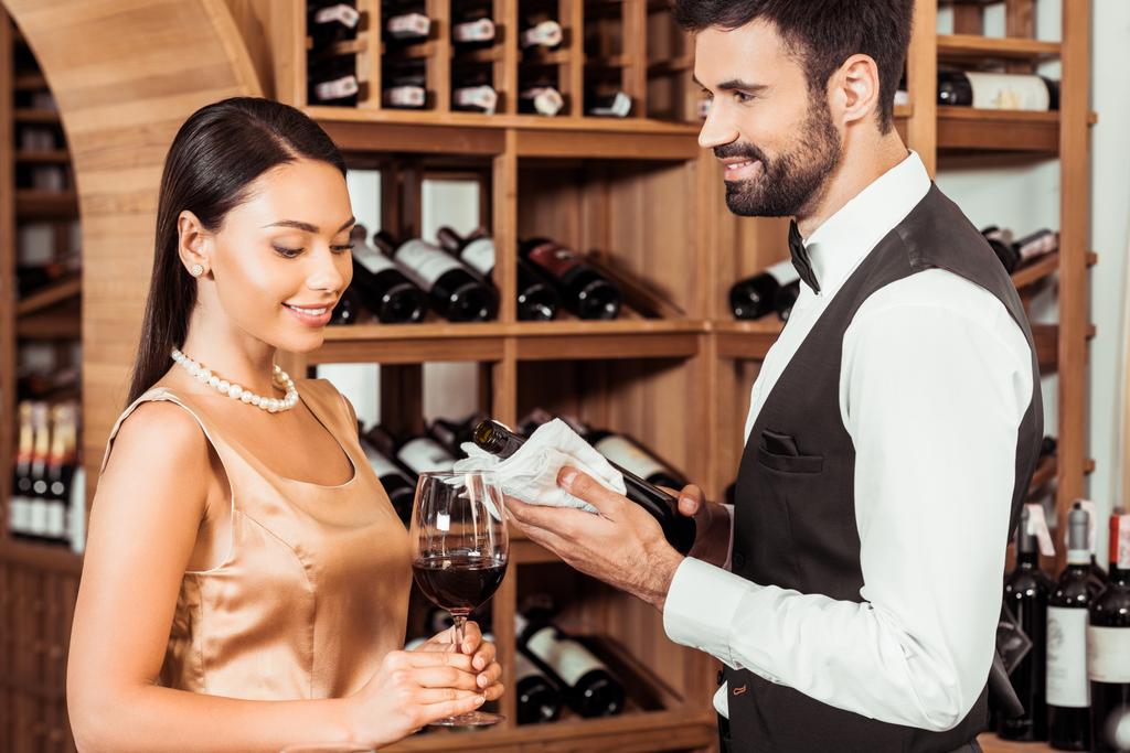 винный управляющий показывает бутылку роскошного вина молодой женщине в винном магазине
 - Фото, изображение