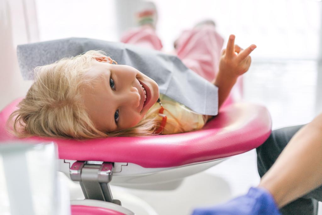 Kinderporträt zeigt Friedenszeichen in Zahnarztpraxis - Foto, Bild