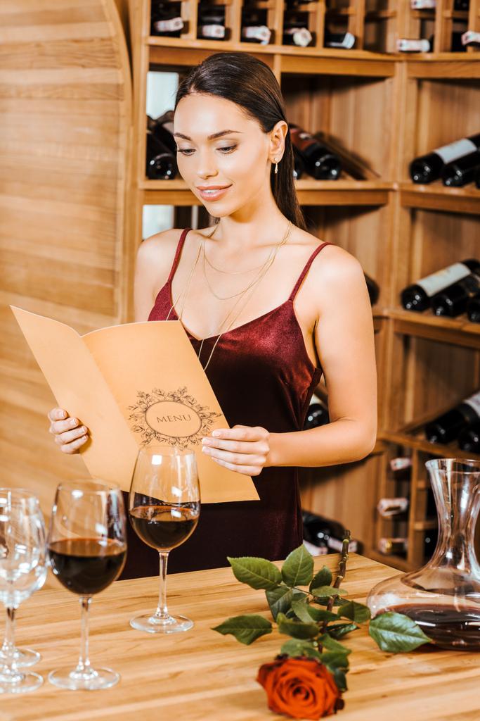 ワインの店でワインのカードを読む赤いドレスで美しい女性 - 写真・画像