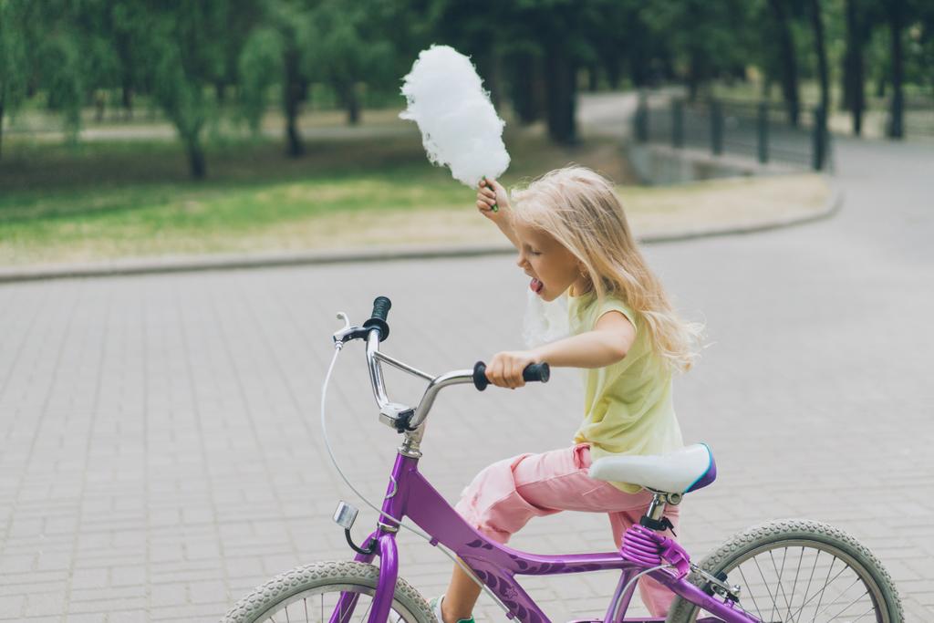 вид сбоку ребенка с хлопковой свечой на велосипеде в парке
 - Фото, изображение