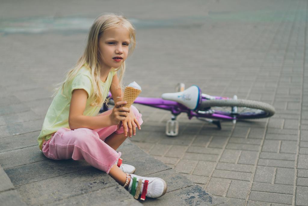 cute child with ice cream sitting on city steps near bicycle alone - Photo, Image