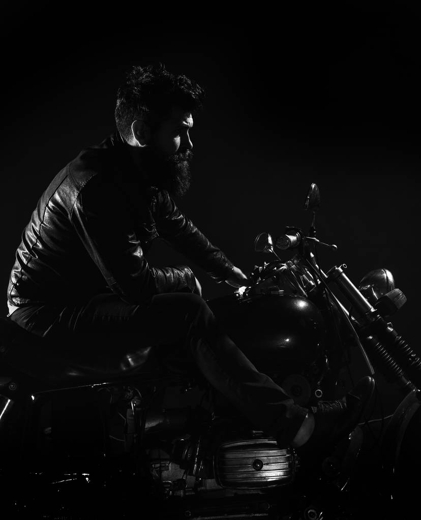 Macho, βάναυση ποδηλάτης στο δέρμα σακάκι μοτοσικλέτα ιππασίας κατά τις νυκτερινές ώρες, διάστημα αντίγραφο. Άνδρας με γενειάδα, ποδηλάτης δερμάτινο σακάκι κάθεται σε μηχανοκίνητο ποδήλατο στο σκοτάδι, μαύρο φόντο. Ποδηλάτες αναψυχής έννοια - Φωτογραφία, εικόνα